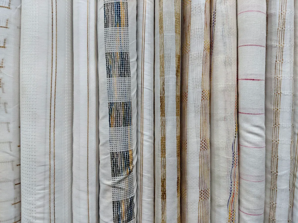 Rollos de tela con patrones finos en tonos crema, ocre y terracota, apilados en una tienda